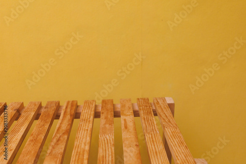 Wooden slats rest on a surface against a yellow wall in a bright space with minimal decor