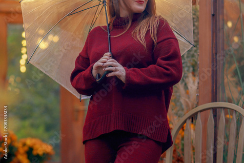 Photos portrait of a female in a cozy knitted sweater holding a clear umbrella, melancholic fall season mood concept
