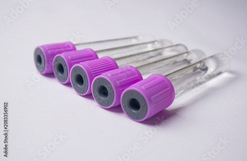 фотографія A high-angle, close-up shot of five empty medical blood collection tubes with purple caps, arranged diagonally on a plain white background