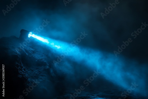 A bright blue flashlight beam cutting through thick dark smoke and fog