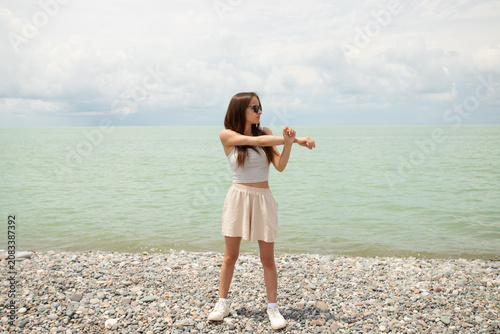teenage girl stretches on a pebble beach by the sea, showing light coastal exercise, summer fitness, warm up before sport and healthy active travel by the water