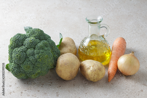 Fresh raw broccoli, potatoes, carrot, onion and olive oil ingredients on light stone background. Healthy vegetables and cooking ingredients for homemade meals and soups
