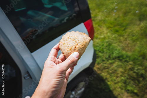 Foto Hand holding homemade biscuit beside parked car with grassy background, warm out