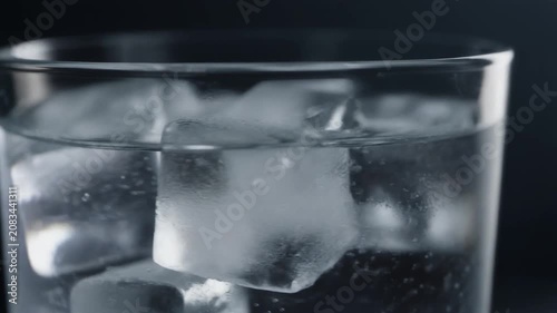 Ultra realistic cinematic footage of clear glass drink with ice cubes rotating slowly, macro, no people, 4K UHD