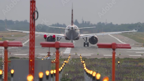 Passenger airplane starting takeoff run on airport runway with glowing approach lights in foreground, telephoto shot with visible heat haze