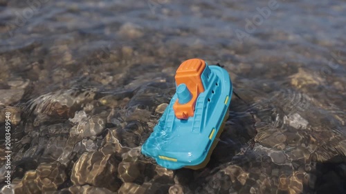 A small toy boat struggles against incoming waves before tumbling in the surf, creating a powerful visual metaphor for fragile childhood dreams challenged by life's obstacles. Slow-motion water