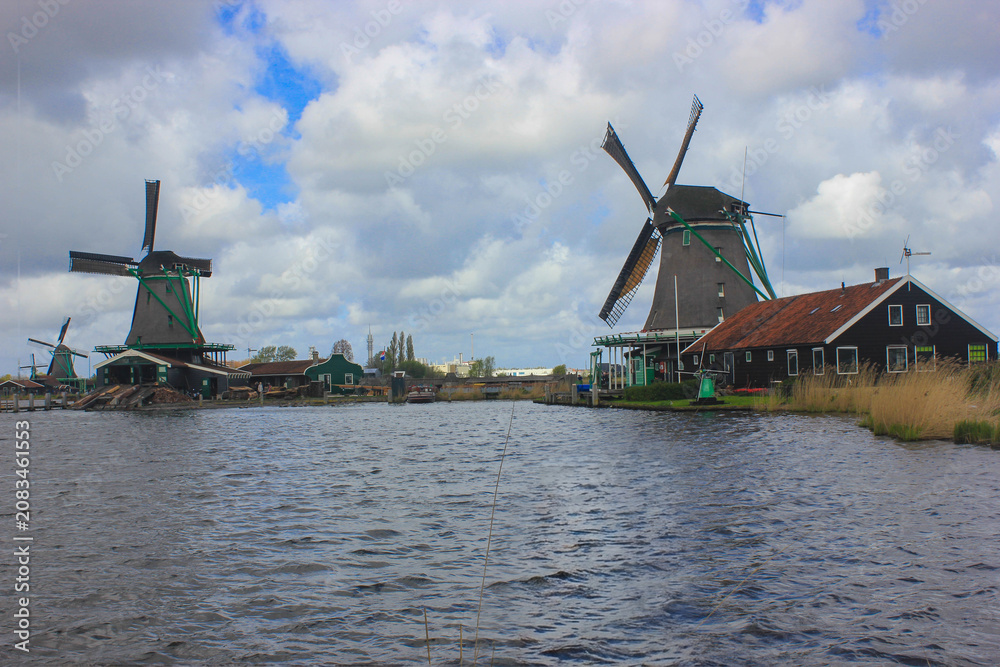 Naklejka premium May 20 2025 Zaanse Schans Netherlands Traditional Historic Wooden Windmills on the Riverbank Under Cloudy Blue Sky