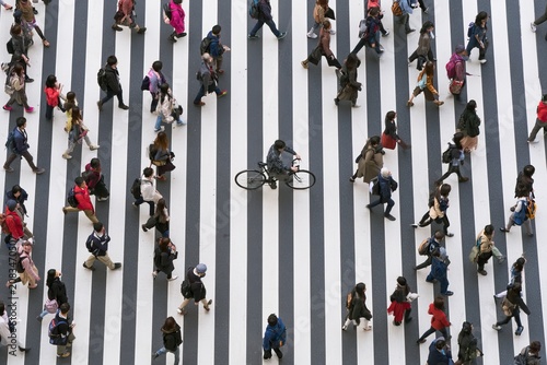 A person on a bicycle navigates a busy crosswalk filled with pedestrians