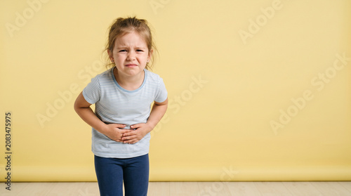 Little Girl Holding Her Stomach With Painful Expression Over Yellow Background