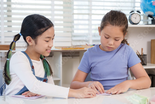 Cuadro en lienzo Asian preteen girl smiles guiding caucasian classmate folding paper during origa
