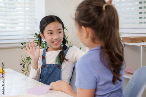 Konstfotografi Asian girl smiles raising hand toward caucasian friend during classroom session