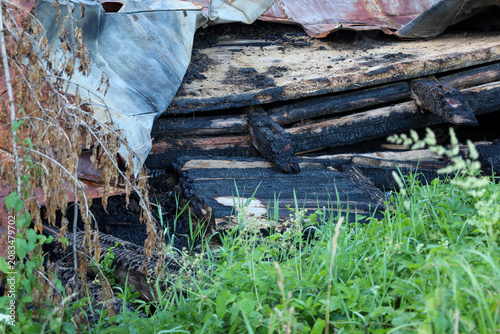 фотографія Burnt wooden beams and destroyed structural elements lie among green grass after a fire