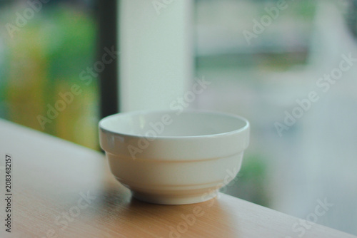 A minimalist white ceramic bowl placed on a digital kitchen scale beside a clear glass, illuminated by soft natural window light. A clean, modern kitchen scene with a calm atmosphere, perfect for food