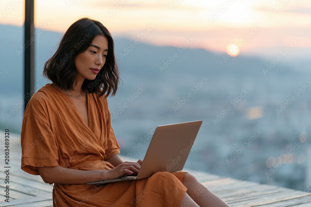 Fototapeta premium Remote work lifestyle woman on a balcony at sunset using a laptop with city skyline view for workspace banner and social media background
