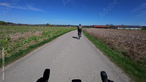 Bicycle point of view footage following a cyclist from the back on a scenic asphalt road through lush green countryside in Bavaria during spring season capturing an active outdoor training ride
