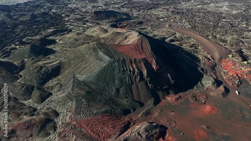 An aerial drone shot orbiting a massive volcanic cinder cone crater, showcasing contrasting black ash slopes and red volcanic soil in El Pinacate Biosphere Reserve, Sonora, Mexico.