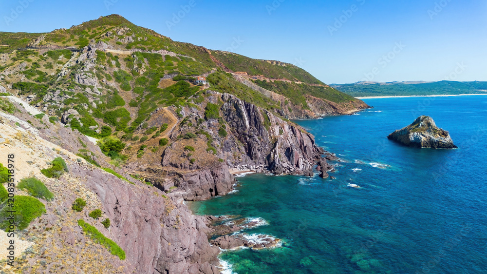 Fototapeta premium Aerial view of the dramatic rocky coastline and cliffs near Nebida, featuring the Spiaggia di Fontanamare in the distance, Sardinia, Italy