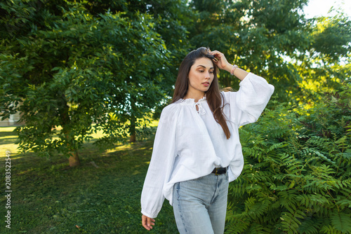 Fotografie A young attractive woman with long brunette hair looking away thoughtfully in a sunny park