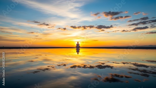 Serene Silhouette Meditating at Golden Sunset Reflection on Calm Water.