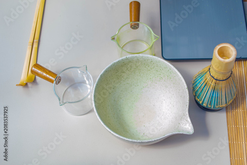Photos Traditional Japanese matcha green tea preparation kit on a table featuring a bamboo whisk chasen on a ceramic holder, ceremonial mixing chawan bowl, and a sifter strainer