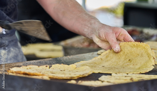 Close-up of hands cooking a traditional corn flatbread on a griddle at a local festival