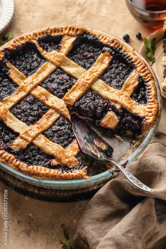 Blueberry pie with lattice crust sliced on brown textured table background close up, traditional homemade dessert