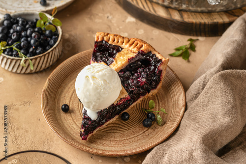 Slice of blueberry pie with a scoop of ice cream on ceramic plate on brown textured table background, traditional homemade dessert