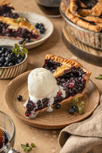 Slice of blueberry pie with a scoop of ice cream on ceramic plate on brown textured table background, traditional homemade dessert