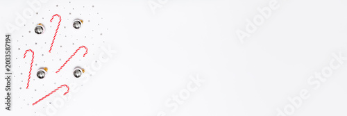 Minimal Christmas background with candy canes, silver baubles and confetti on white copy space for festive banners, ads, sales and social media designs.