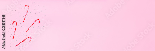 Pink holiday background with candy canes and silver stars on left side, leaving wide copy space for festive banners, sales, greetings and seasonal promo designs.