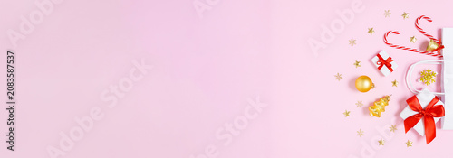 Christmas gifts, candy canes and festive ornaments in white paper bag on pastel pink background with wide copy space for holiday banners, ads and seasonal design layouts. Flat lay.