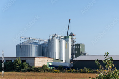 Grain Storage Facility With Silos, Crane and Buildings Located in an Agricultural Area Under a Clear Blue Sky During Daylight Hours
