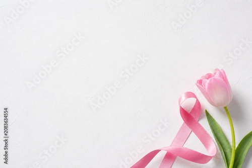 Pink October: Pink ribbon and tulip on textured white background with copy space, hope and prevention concept.