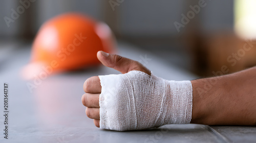 Injured Hand with Bandage and Safety Gear in Background, Illustrating Workplace Accident or Safety Concern