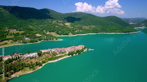 Colle di Tora Turano Lake Italy 4K Drone. Distance fly in approach revealing emerald water lake and long peninsula borgo town from above. Borghi piu belli d Italia most beautiful villages Hidden gems