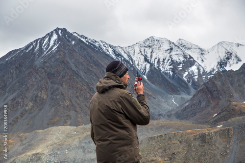 Photography A man holding a two-way radio, with mountains in the background.