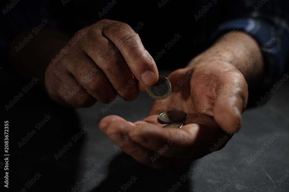 Fototapeta premium Poverty. Homeless senior man counting coins at table in darkness, closeup