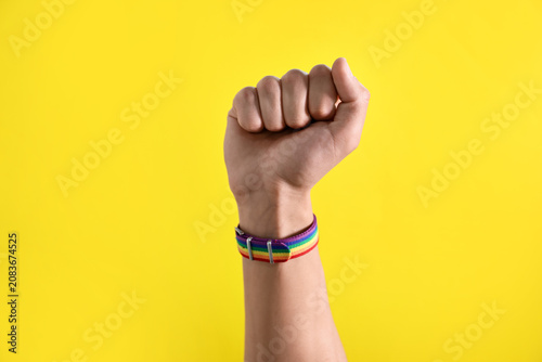Photos Man wearing wristband in LGBT colors and showing fist on yellow background, clos