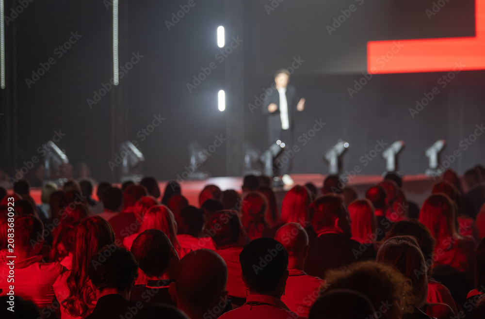 Obraz premium Speaker captivates an audience during dynamic conference presentation with striking red lighting.