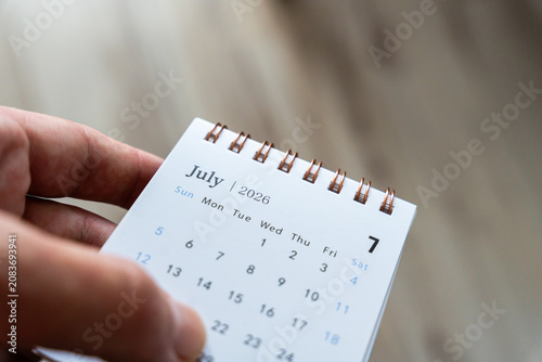 Hand holding a calendar page displaying July 2026, symbolizing planning and organization for the upcoming month, perfect for personal productivity or time management themes.