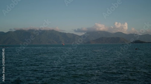  Nha Trang Vietnam coastal panorama with deep teal water, distant layered mountains, small boats, broad horizon, soft daylight