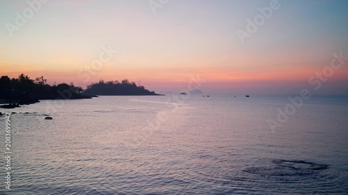 Nha Trang Vietnam. 01 06 2026 Panoramic coastal sunrise over calm sea with silhouetted headland, anchored boats, pastel sky, gentle reflections, rocky