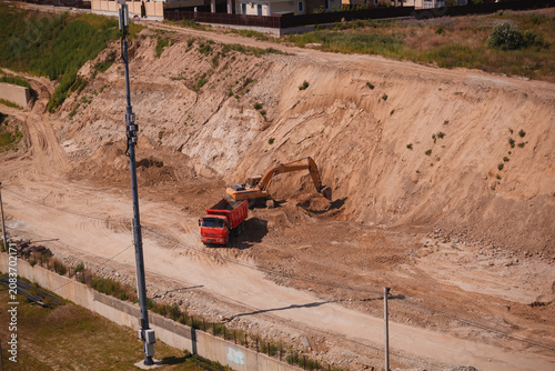 Yellow excavator loading dirt into a red dump truck at a construction site quarry