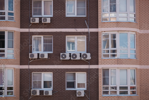 Modern brick residential building facade with multiple air conditioner units installed outside