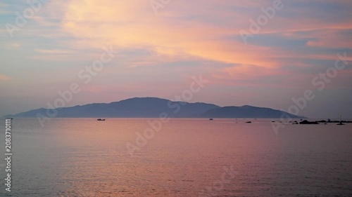 Nha Trang Vietnam. Calm tropical seascape at sunrise with silhouetted island ridge, small fishing boats, pastel cloud reflections, wide horizon