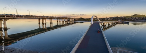 Fotografía A scenic view of the Nga Hau Mangere Bridge in Onehunga, Auckland, New Zealand, at sunset, with traffic on the adjacent bridge reflecting in the calm water