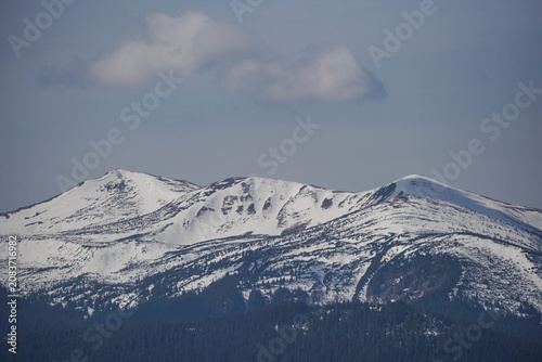 Majestic snow covered mountain ridge under a blue sky with soft white clouds in spring.