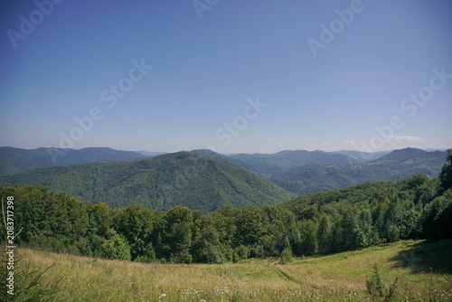 Scenic landscape of green rolling mountain hills and dense forest under clear blue sky in summer.