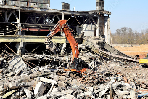 A modern excavator with hydraulic shears removes building debris.