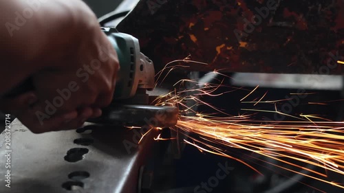 Close-up of a worker operating an electric angle grinder on a steel structure, producing a stream of bright sparks in a workshop